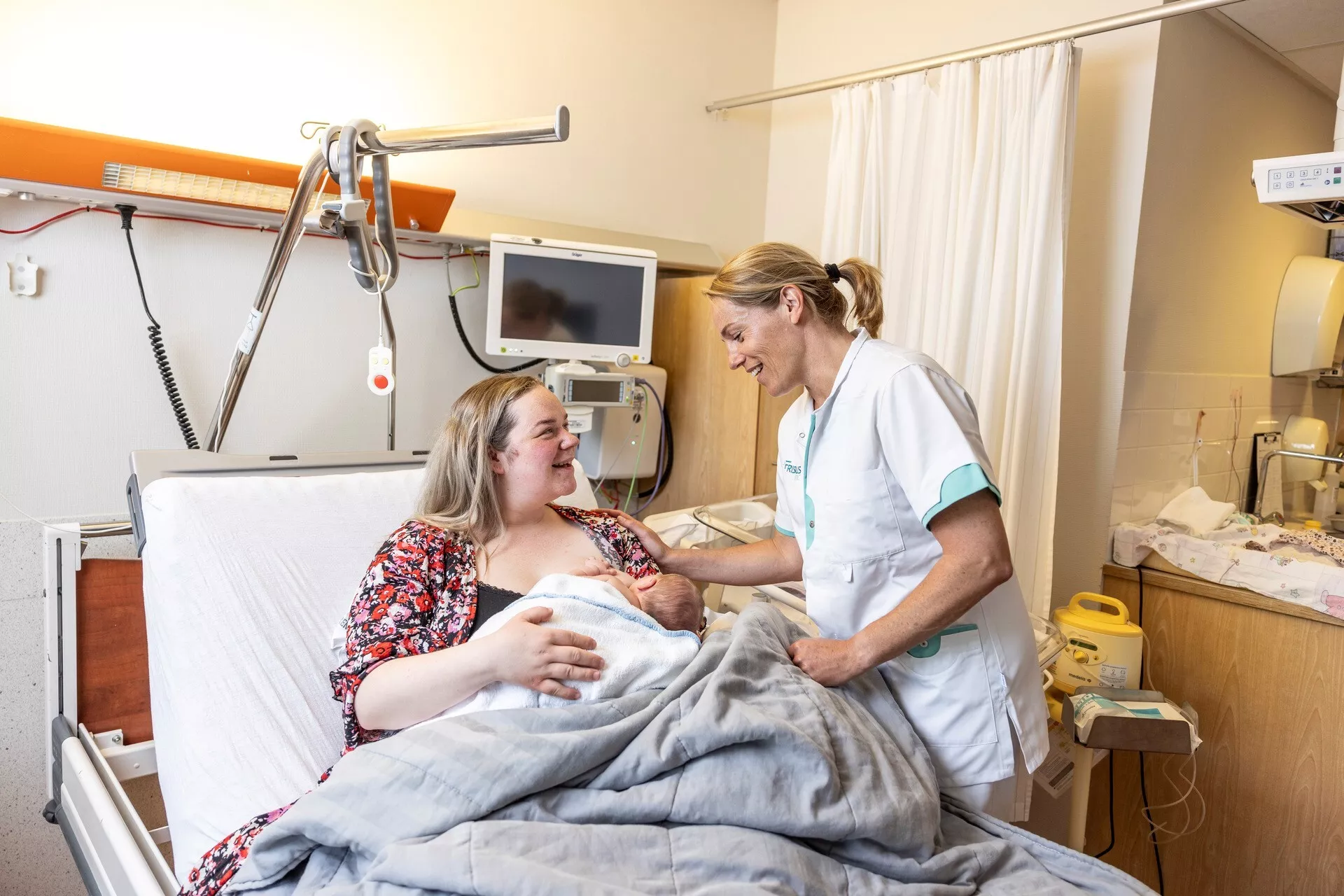 Een vrouw in een ziekenhuisbed met haar pasgeboren baby en een zorgverlener.