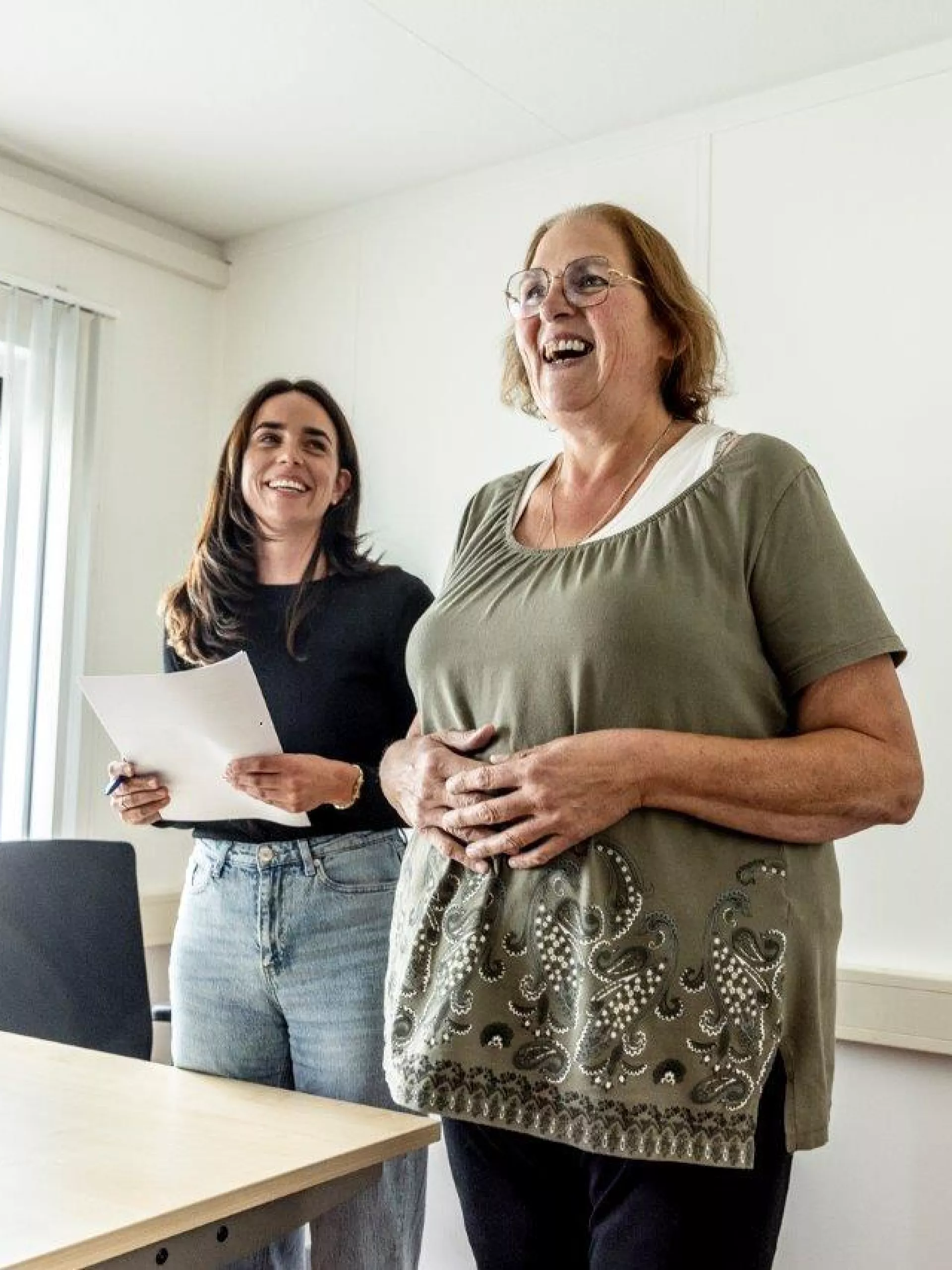 Twee vrouwen lachen in een kantooromgeving.