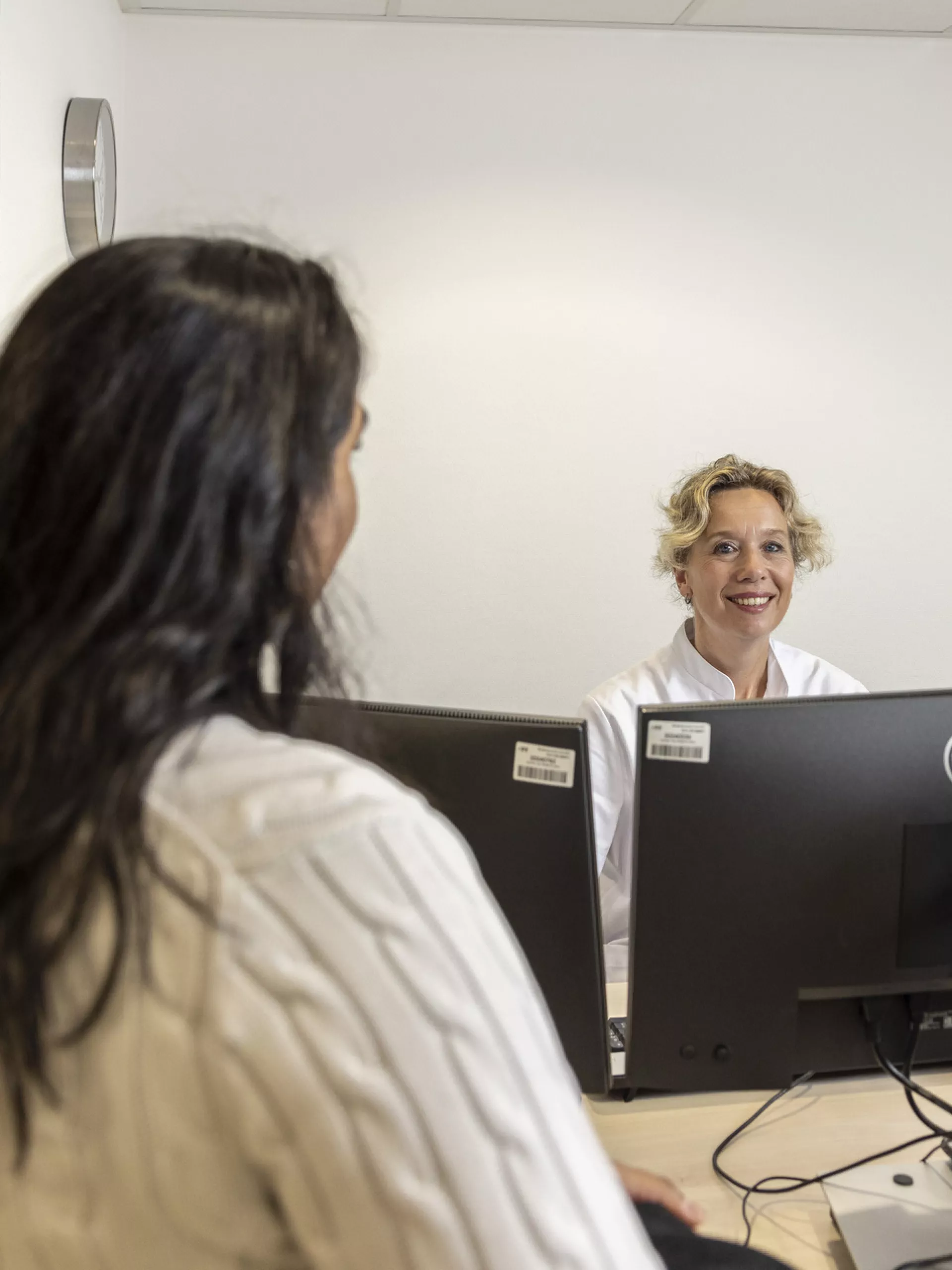 Twee vrouwen in gesprek bij een balie in een kantooromgeving.