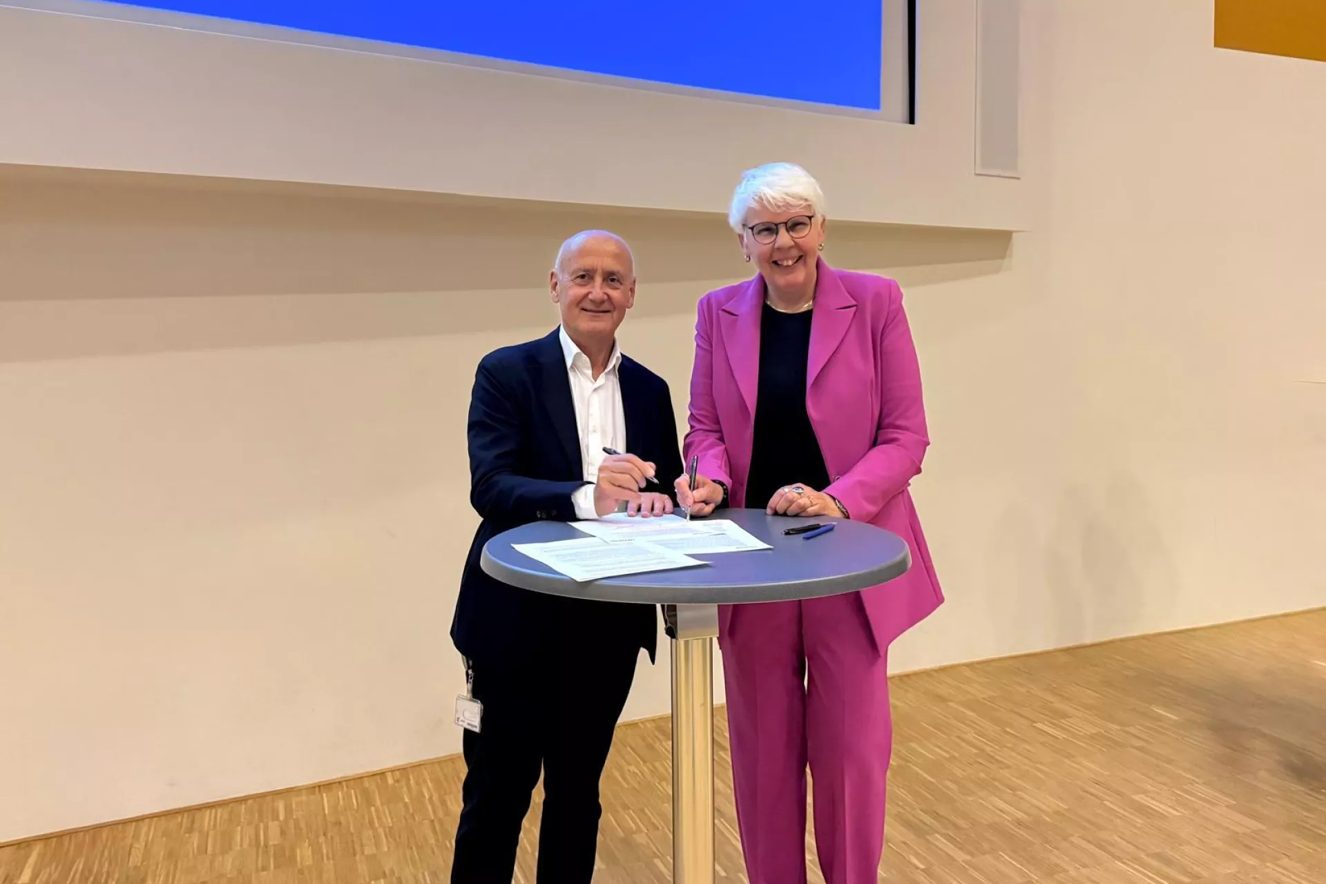 Twee bestuurders poseren samen bij een hoge tafel bij een ondertekenmoment.